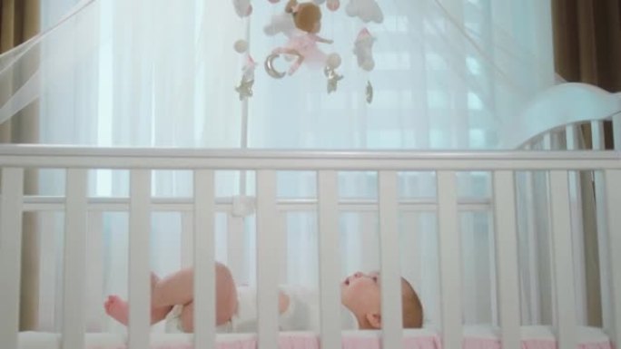 迷人可爱的女婴，躺在婴儿床上，专注于婴儿床玩具。在阿里·阿列克谢迷你上拍摄。