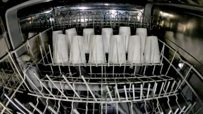 塑料盘子在洗碗机中清洗。疯狂的想法是在洗碗机里洗塑料眼镜。查看洗碗机和塑料一次性餐具。慢动作内部视图