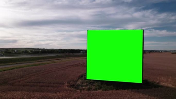 日落时繁忙的高速公路或高速公路附近带有绿屏的大广告牌的空中无人机镜头