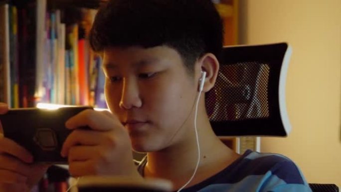亚洲少年男孩在晚上在家玩手机游戏，生活方式概念。