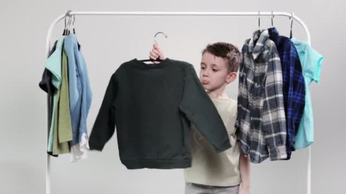 男孩学龄前儿童站在衣架旁边，收拾衣服，为今天选择衣服。