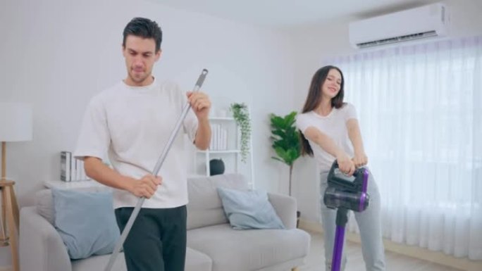 白人年轻男女一起在家打扫客厅。美丽可爱的男女夫妇跳舞，一边用吸尘器打扫脏乱的肮脏地板，做家务和家务。