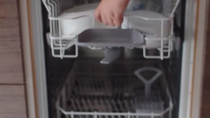 十几岁的男孩从洗碗机里拿干净的盘子。年轻人用手特写镜头卸下洗碗机。帮助妈妈。年轻人把装有脏盘子的最上