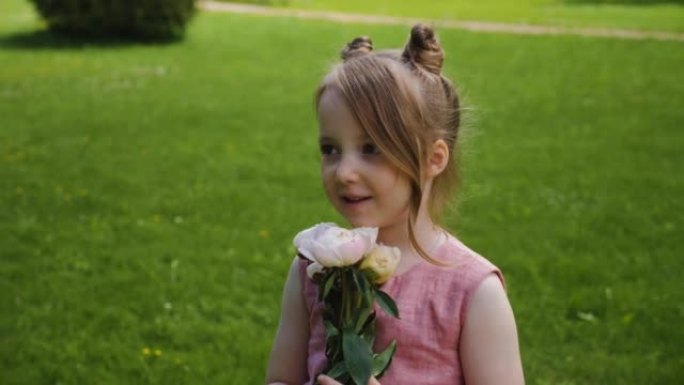 穿着粉红色连衣裙的美丽女婴在大自然的绿色草地上站着一束牡丹花