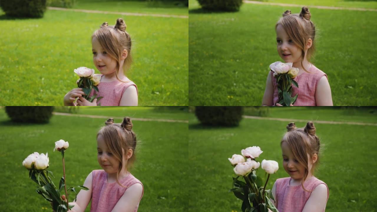 穿着粉红色连衣裙的美丽女婴在大自然的绿色草地上站着一束牡丹花