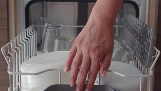家庭主妇把脏盘子放在洗碗机里。女性双手在特写镜头中卸下洗碗机。家用现代家用电器。女人把装有脏盘子的顶