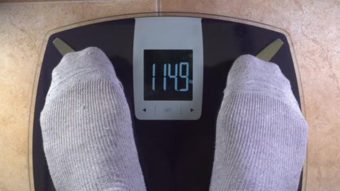 一个穿着灰色棉袜的男人踩在秤上。需要减轻重量的概念。肥胖危险。观点。