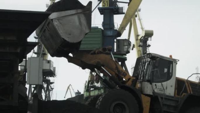带有大型铲斗的装载机将煤装载到传送带上，以运送到海船。海港背景下的技术运输