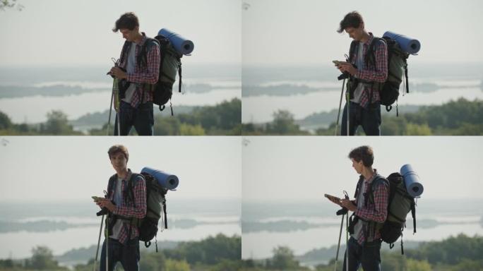 20多岁的男子一大早就带着旅游背包和登山杖在河边徒步旅行。使用智能手机寻找路线的人。