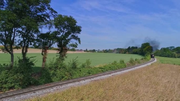 从鸟瞰图上可以看到，一辆古旧的蒸汽客运列车绕过弯道，吹着烟和蒸汽，在黄金时间穿过肥沃的玉米田