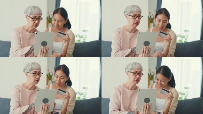 快乐的亚洲家庭，年轻的女儿和年长的妈妈教年长的妈妈使用数字平板电脑在线购物使用信用卡支付在线应用在家