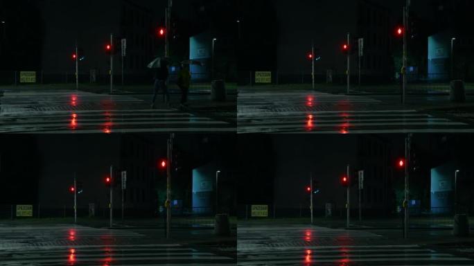 夜城下雨。交通信号灯是红色的。打着雨伞的人沿着人行横道行走。