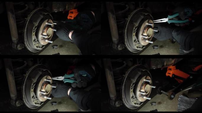 在车间里，一位男性机械师通过灯笼的灯光预见了汽车上轮毂和制动盘的修理。修理制动盘时，机械师用钳子夹紧