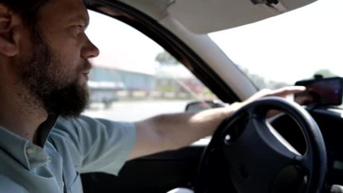 一个大胡子的人坐在汽车的方向盘上，在出租车导航员的帮助下选择旅行路线