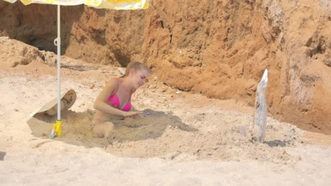 在海滩上休息。一个年轻女孩从沙子里挖了脚。一个美丽的女人被埋在海滩上的沙子中，直到腰部，她用手将沙子