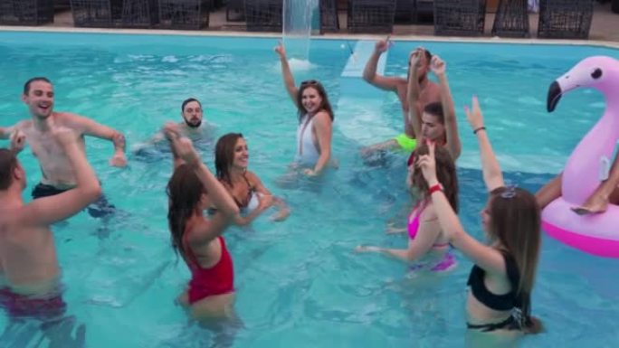 朋友在私人别墅游泳池举行夜间泳池派对。穿着泳装的快乐年轻人在豪华度假胜地泼水，与漂浮物和充气床垫跳舞