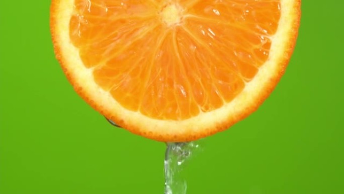 水从绿色背景上的橙色色调橙色落下。橙片和水飞溅，果汁从多汁的水果中掉落。制作水果鸡尾酒，喝冷柠檬水