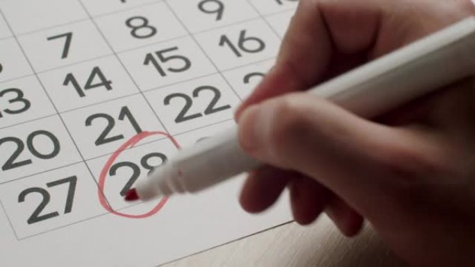 人的手用红笔在纸质日历上写下第28天。