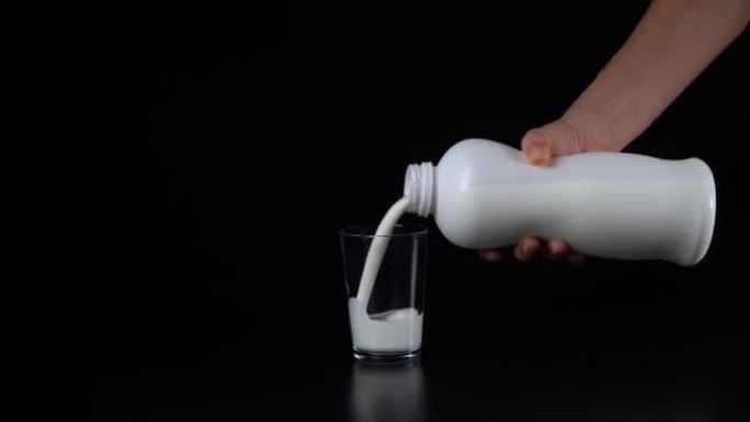 手将牛奶或开菲尔从黑色背景上的塑料白色瓶子倒入玻璃玻璃杯中。