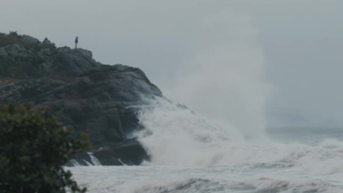 人站在岩石上，看着巨浪在海洋风暴中冲破岩石