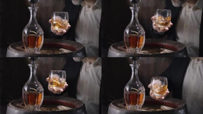 穿着西装和胡须的男人 (侍酒师) 从老式威士忌酒桶中拿出一杯冰上的威士忌，然后摇动玻璃杯以散发出威士