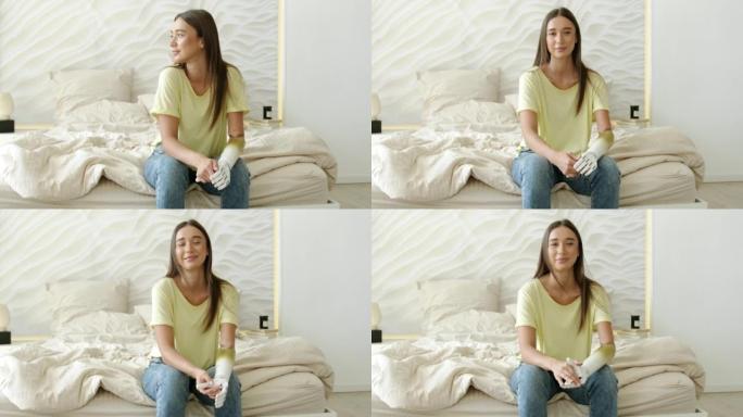 肖像微笑的快乐女人用假肢坐在家里的床上，残疾女孩用假肢。