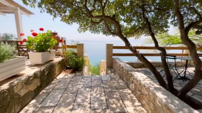 漫步在希腊地中海沿岸美丽的餐厅露台上。海滨露台，植被和鲜花以楼梯结束，这些楼梯下降到清澈的绿松石海中