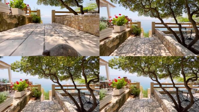漫步在希腊地中海沿岸美丽的餐厅露台上。海滨露台，植被和鲜花以楼梯结束，这些楼梯下降到清澈的绿松石海中