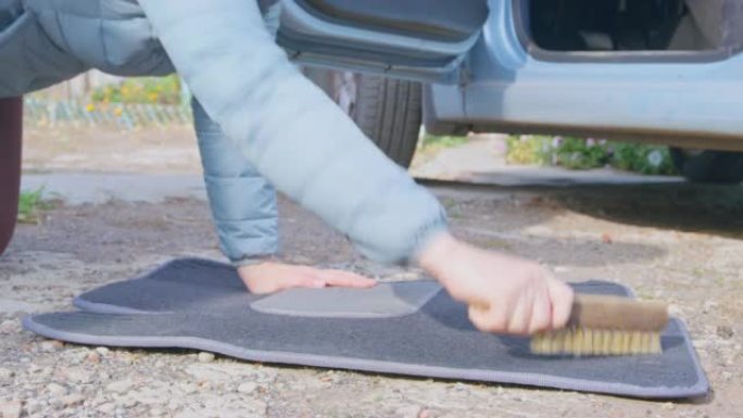 人用木柄上的硬刷清洁汽车地毯上的灰尘