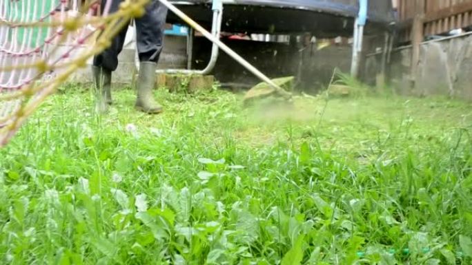 男子使用手动燃气机器在院子里修剪高草