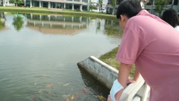 亚洲青少年男孩和女孩看着池塘里的鸭子和鲤鱼，同时一起在公园户外放松，生活方式的概念。