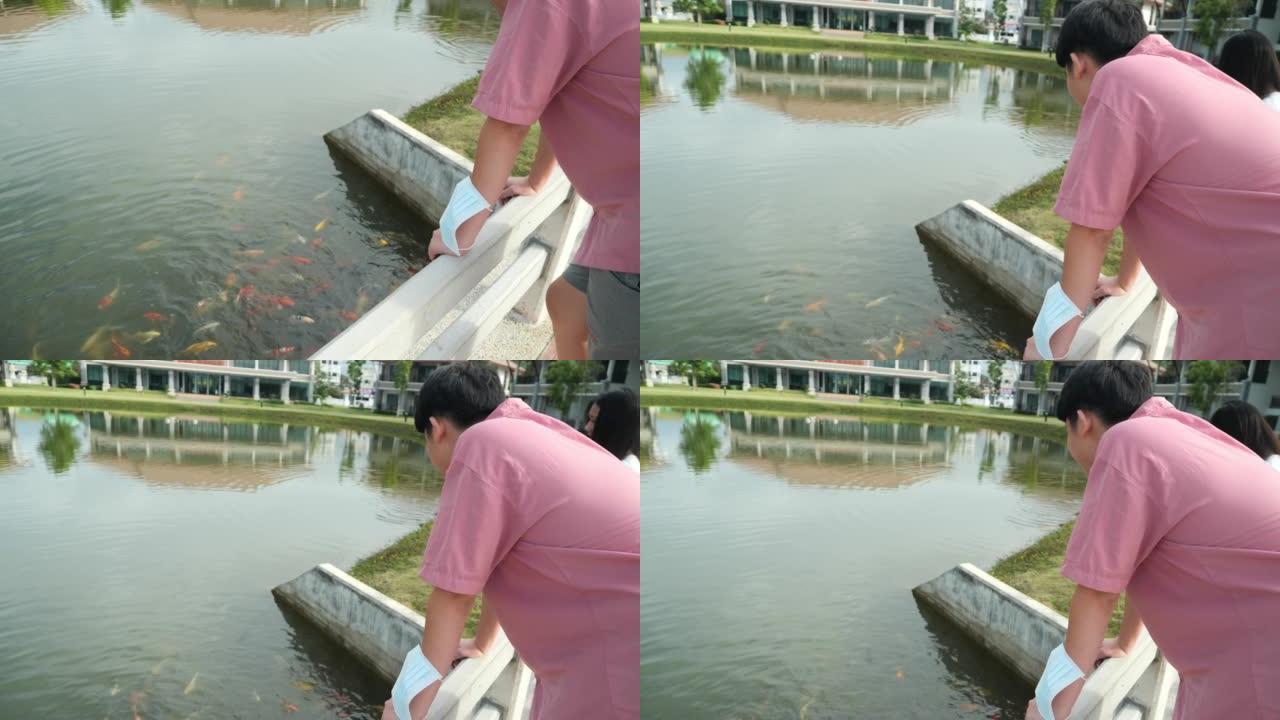 亚洲青少年男孩和女孩看着池塘里的鸭子和鲤鱼，同时一起在公园户外放松，生活方式的概念。