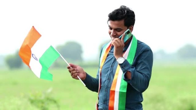 农民在绿色的田野上用手机通话，手里拿着国旗