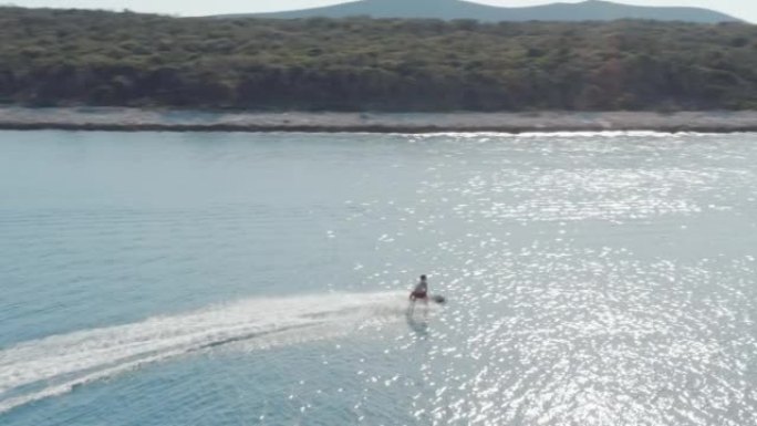 穿着红色泳衣的男子在平静的海水上骑着电动喷气式冲浪板的航拍画面。炎热的夏日，享受水上运动。游艇上的豪