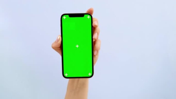 女人手持带有空白绿色屏幕的智能手机，展示应用程序或网站设计的复制空间，站在蓝色工作室背景下，模型素材