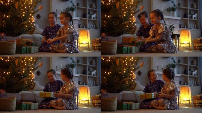 两个兴奋的女孩坐在地板上的圣诞树下拿着礼品盒