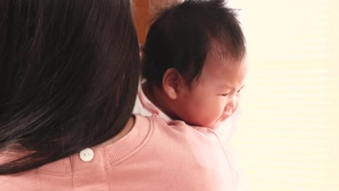 亚洲新生婴儿被妈妈抱在肩上，母亲的生活方式在家照顾婴儿，好奇的小女孩与无辜的孩子环顾四周，快乐的女人