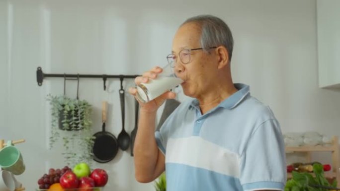亚洲高级成熟男性在家厨房喝一杯牛奶。有吸引力的年长的祖父在早上醒来后抱着一杯牛奶，在家里做保健。