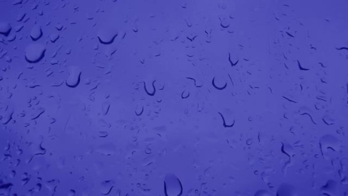 自然玻璃背景的窗户。玻璃上蓝色水滴的特写镜头，雨。在夏天，秋天的倾盆大雨中，大滴雨落在窗户玻璃上。