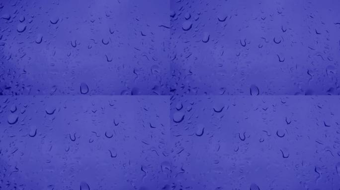 自然玻璃背景的窗户。玻璃上蓝色水滴的特写镜头，雨。在夏天，秋天的倾盆大雨中，大滴雨落在窗户玻璃上。