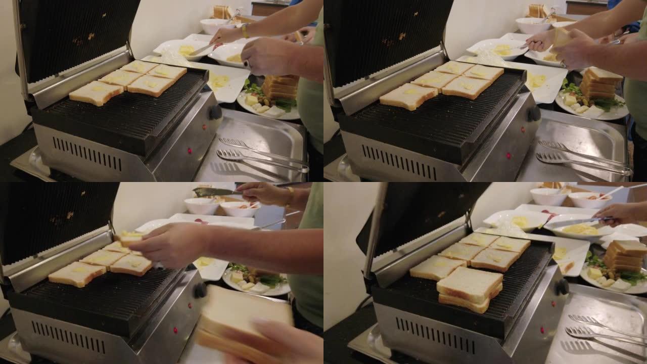 制作三明治的电烤架。一个人在自助食堂准备三明治。