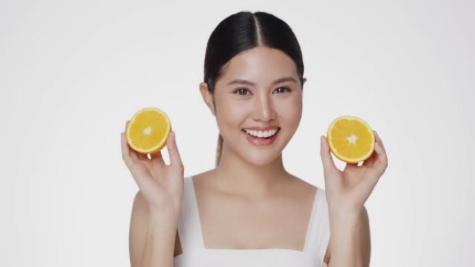 亚洲女性对完美清洁健康的皮肤感到满意。可爱的女模特干净清新的皮肤拿着一个橙色。富有表现力的面部表情。