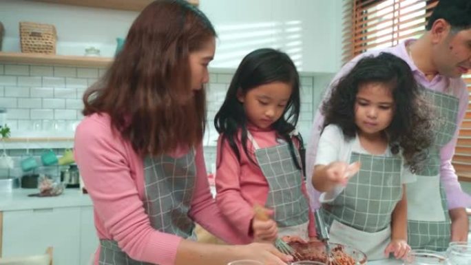 亚洲新手父母正在厨房教女儿上烹饪课。