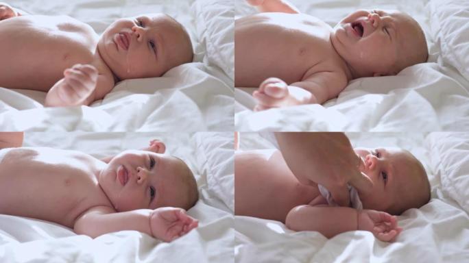 婴儿反流母乳。小婴儿哭泣，妈妈清理她可爱的脸。可爱的新生婴儿的真实特写镜头。童年的概念，新生活，母乳