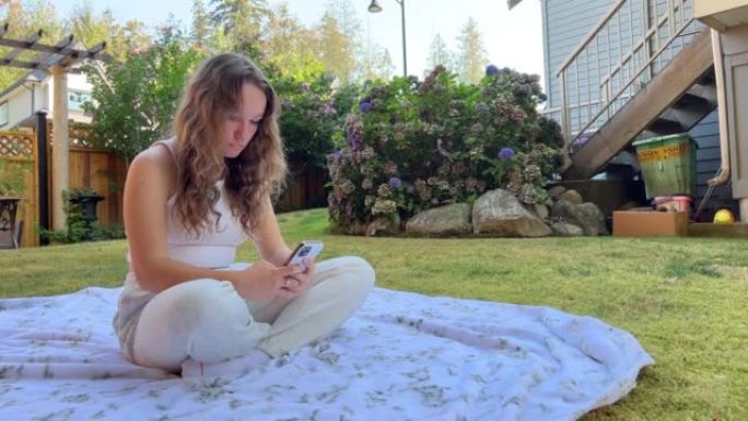 一个十几岁的女孩坐在大自然中，但没有把目光从电话上移开。她坐在社交网络Facebook Instag
