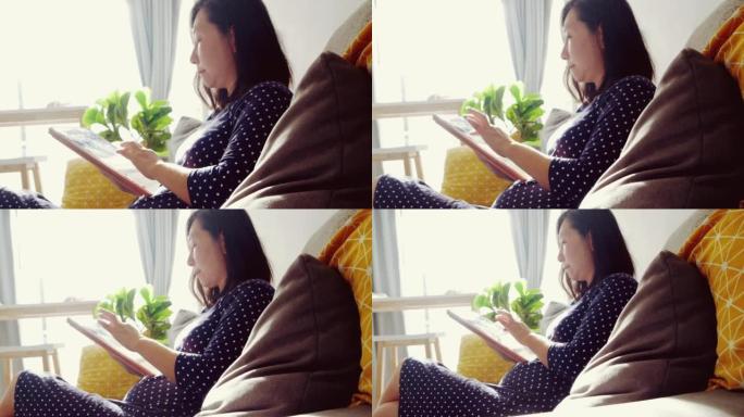 Asian adult woman using digital tablet on sofa at 