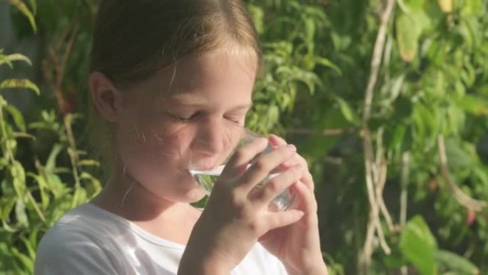 小女孩在绿色背景的户外玻璃上喝水
