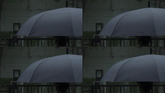 灰色雨伞上的雨。曼谷晚上雨中的银伞。镜头雨滴落在雨伞上。代表恶劣天气冬季雨季或保护。雨中的人和雨伞。