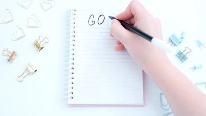 女性手在白色背景特写的笔记本上写下目标。