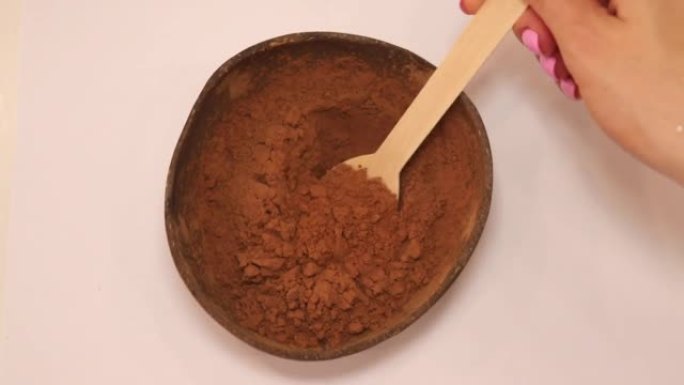 可乐碗里的角豆粉。拿起一勺角豆树喝一杯热饮。